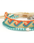 A set of three beaded bracelets stacked together on a white background. The top bracelet is made of cream cord with a small silver heart charm.