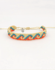 A beaded adjustable friendship bracelet with a cream-colored cord and a geometric pattern of orange, turquoise blue, and cream seed beads, featuring a small silver metal charm.
