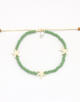 A beaded bracelet with green round beads, three cream starfish charms, and a cream adjustable cord closure with small brown beads at the ends, shown on a white background.