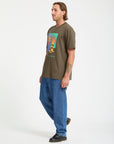 Man wearing a green t-shirt with a colorful graphic and blue jeans on a white background