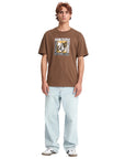 Person wearing a brown t-shirt with a logo and text, standing against a white background