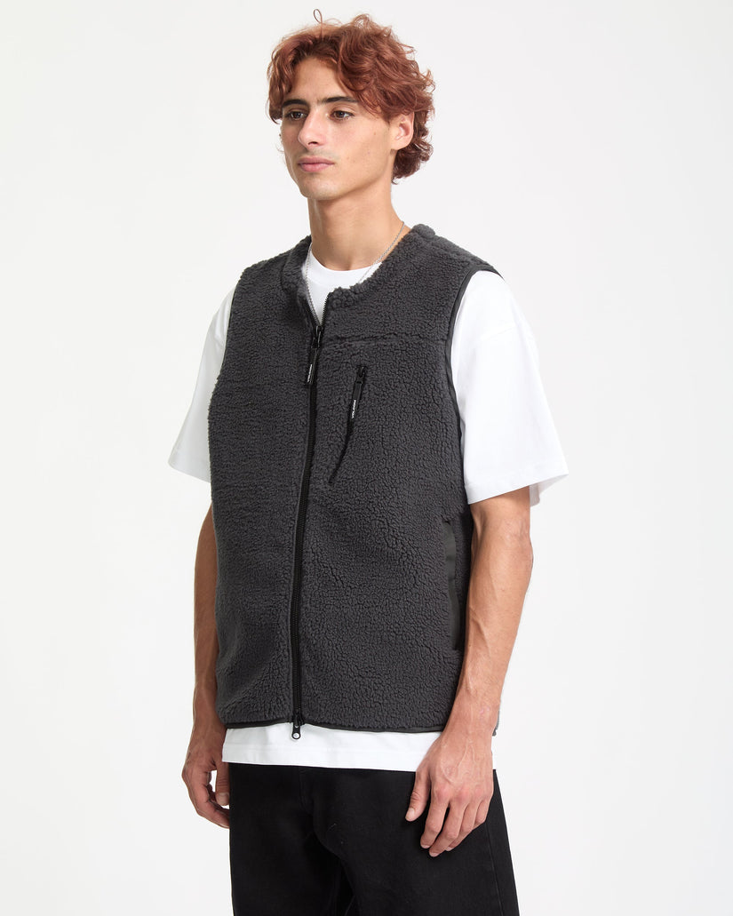 Man wearing a black textured vest over a white shirt on a white background