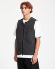 Man wearing a black textured vest over a white shirt on a white background