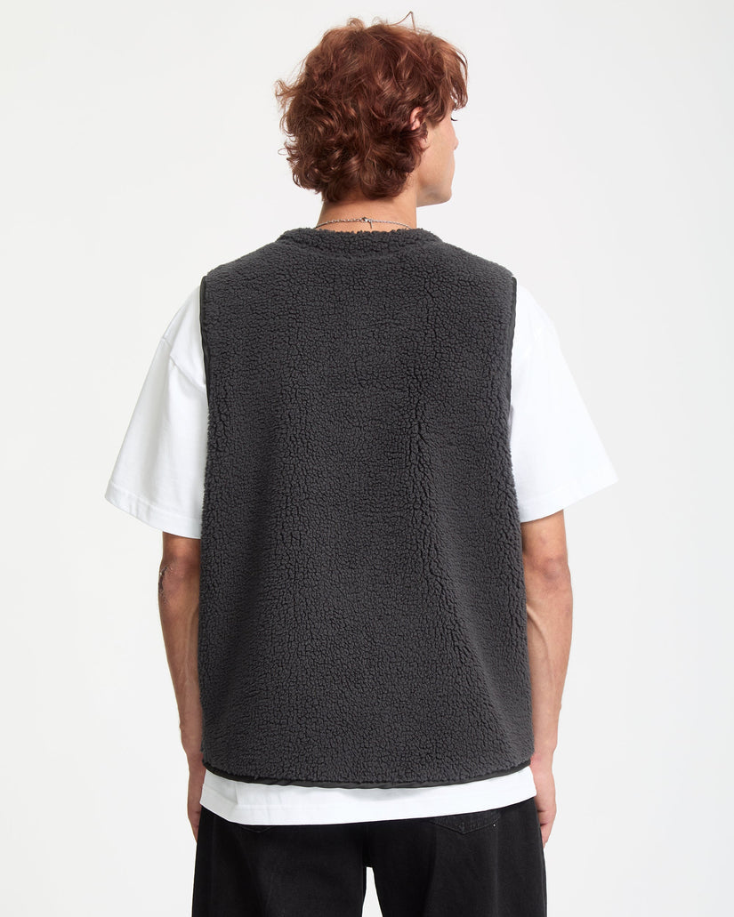 Person wearing a dark gray fleece vest over a white shirt on a white background