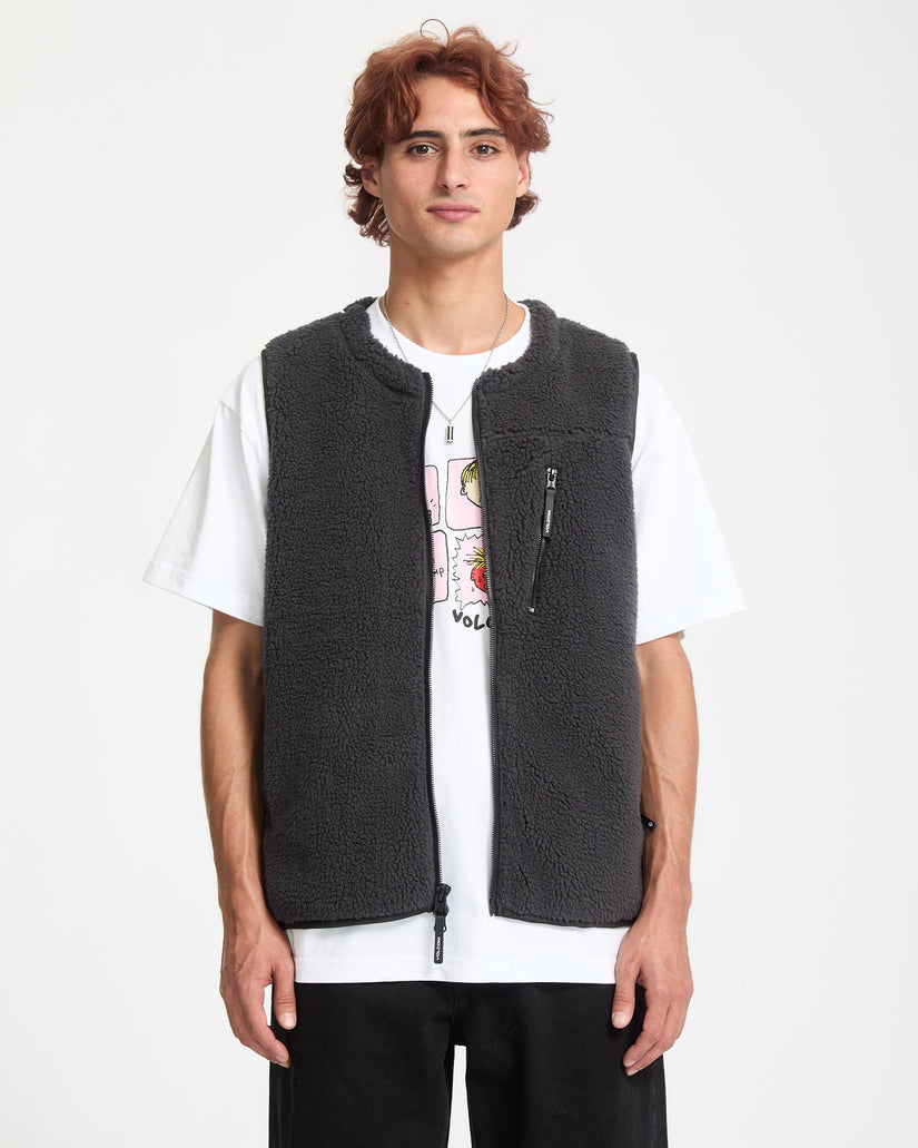 Person wearing a dark gray fleece vest over a white t-shirt with graphic designs on a white background