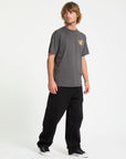 Man wearing a gray t-shirt with a logo and black pants on a white background