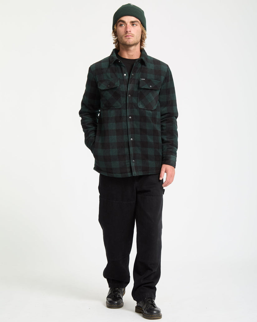 Man wearing a green plaid shirt and black pants on a white background