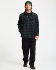 Man wearing a green plaid shirt and black pants on a white background