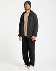 Man wearing a black hoodie, beige shirt, black pants, and white sneakers on a white background