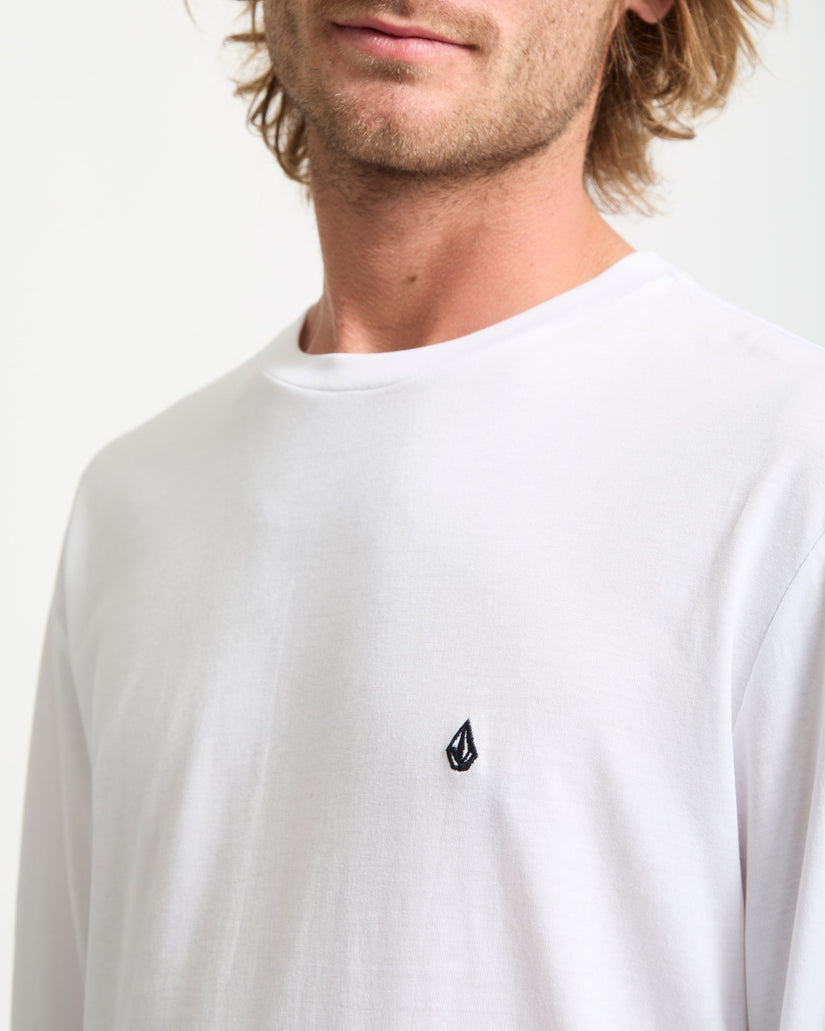 Man wearing a white long-sleeve shirt with a small logo on a plain background