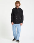 Man wearing a black button-up shirt and light blue jeans on a white background