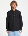 Man wearing a black button-up shirt with a small logo on a white background