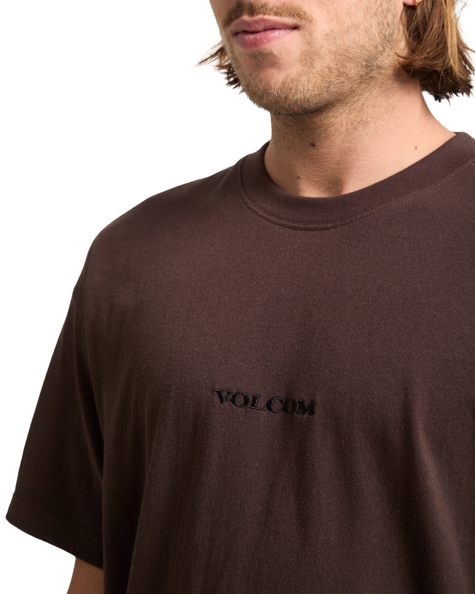 Man wearing a brown t-shirt with 'Volcom' logo on a white background