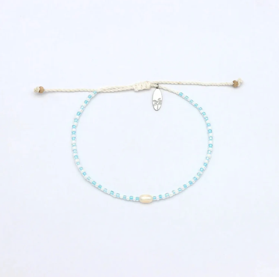 A delicate beaded cord bracelet with light blue and white beads, a central cream-colored bead, and a small silver metal charm, displayed on a clean white background.