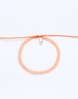 A peach-colored beaded bracelet with a matching adjustable orange cord and a small silver-toned metal charm, displayed on a clean white background.