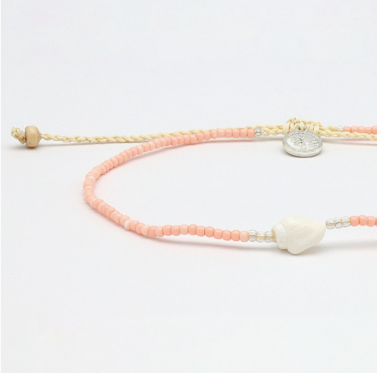 A delicate beaded bracelet with peach-pink and cream-colored beads, featuring a white shell charm, silver spacer beads, and a round silver metal charm, displayed on a clean white background.