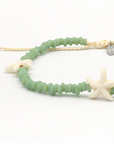 A beaded necklace with light green round beads, a cream braided cord, a white starfish charm, and a small silver star-shaped charm on a white background.