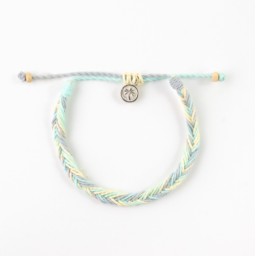 A braided cord bracelet in pastel mint green, light blue, and pale yellow, featuring a small silver-toned circular charm with a palm tree design, displayed on a clean white background.