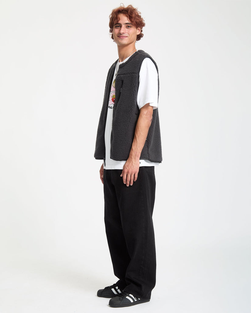 Person wearing a gray vest over a white shirt with a graphic design, black pants, and black shoes on a white background
