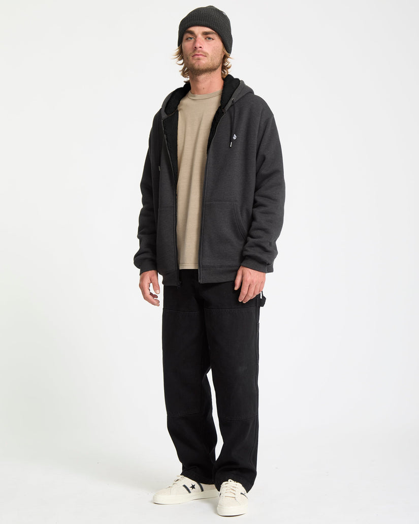 Man wearing a black hoodie, beige shirt, black pants, and white sneakers on a white background