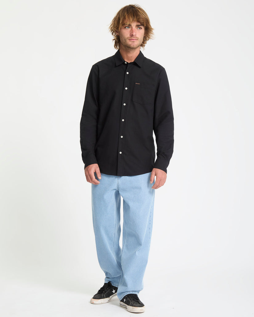 Man wearing a black button-up shirt and light blue jeans on a white background