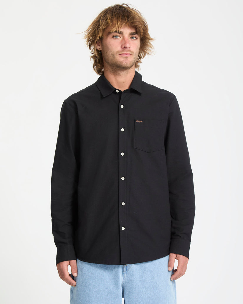Man wearing a black button-up shirt with a small logo on a white background